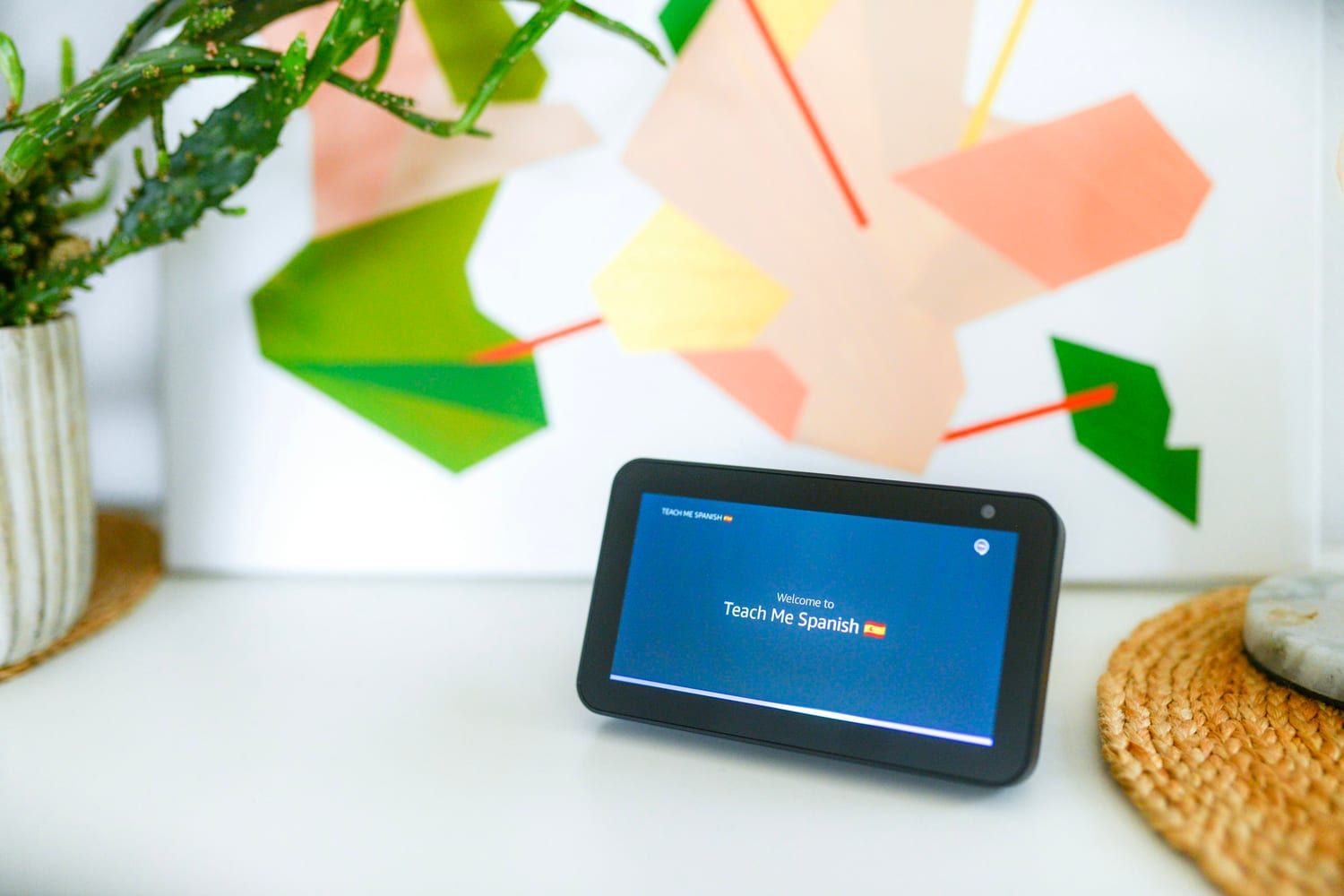 Una pantalla Echo Show encendida sobre un mueble blanco, junto a una planta