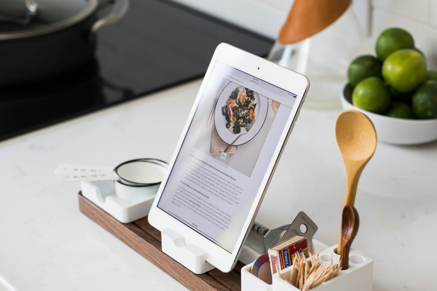 Un iPad con una receta en pantalla, apoyado en un soporte de madera junto a los utensilios de cocina