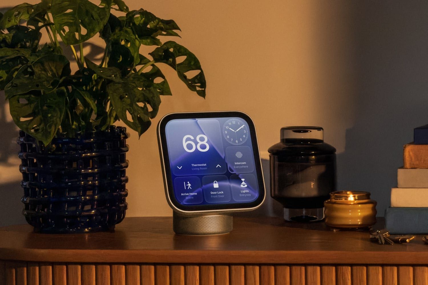 Un Apple HomeView sobre un mueble de madera, junto a una planta y una vela