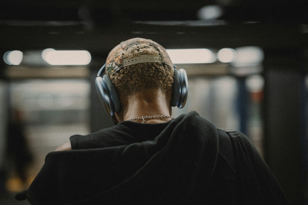 Una persona de espaldas con auriculares de diadema en el andén del metro