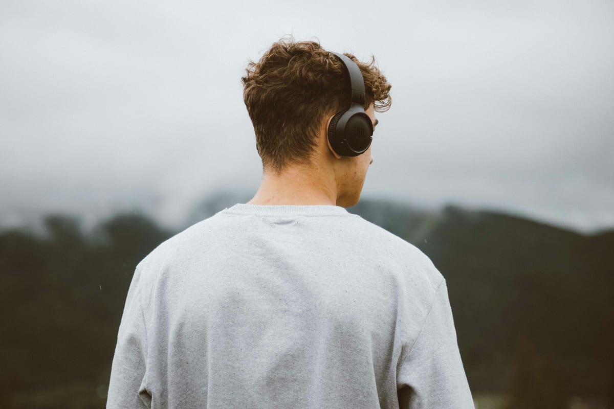 Un hombre de espaldas con auriculares mirando unas montañas con niebla