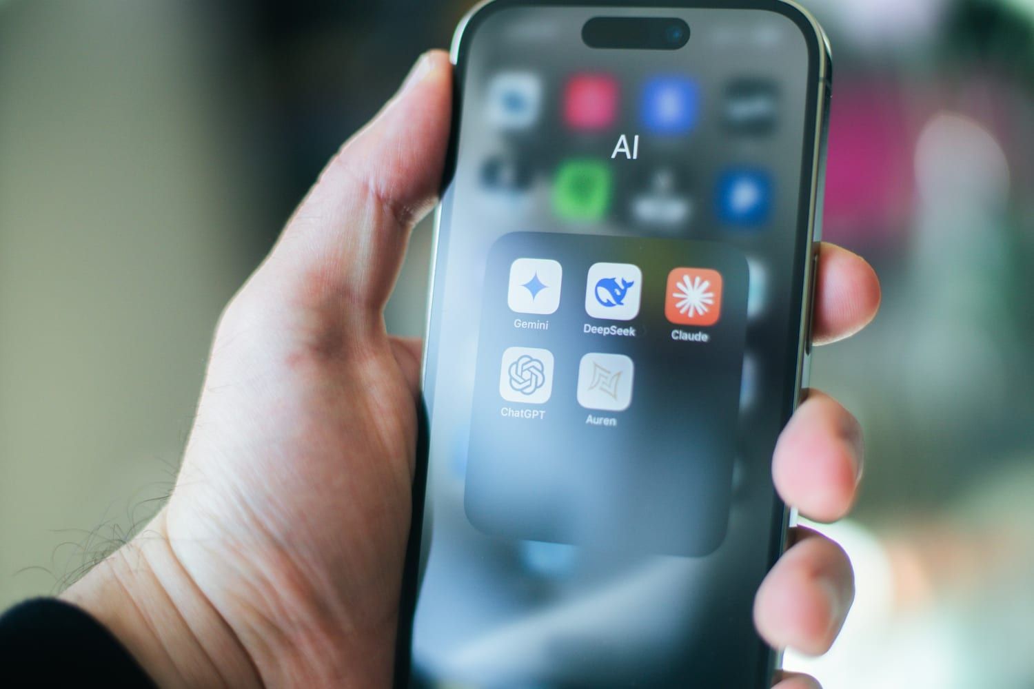 Una mano sujeta un móvil con una carpeta de aplicaciones de IA: Gemini, DeepSeek, Claude y ChatGPT