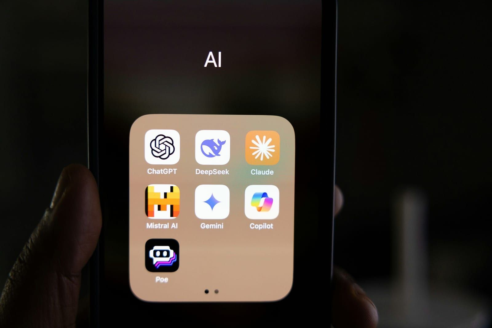 Una mano sostiene un móvil con una carpeta de apps de inteligencia artificial: ChatGPT, DeepSeek, Claude, Mistral, Gemini y Copilot