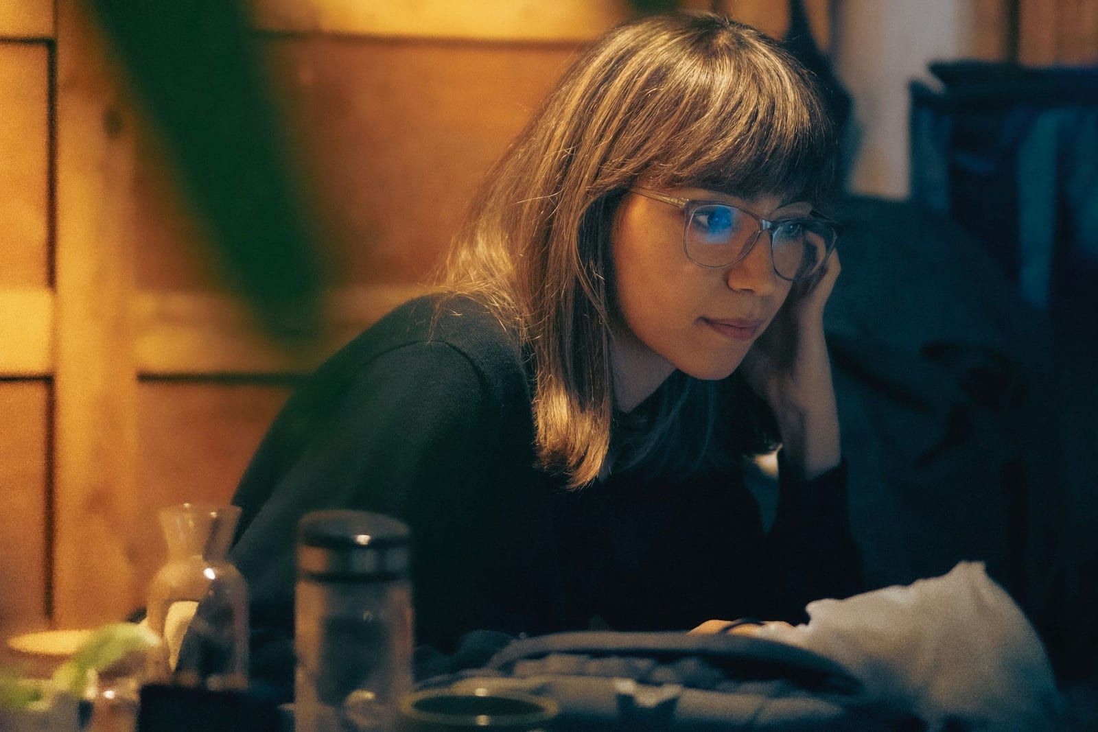Una mujer con gafas mira la pantalla de su portátil de noche, con la cara apoyada en una mano y una luz cálida al fondo