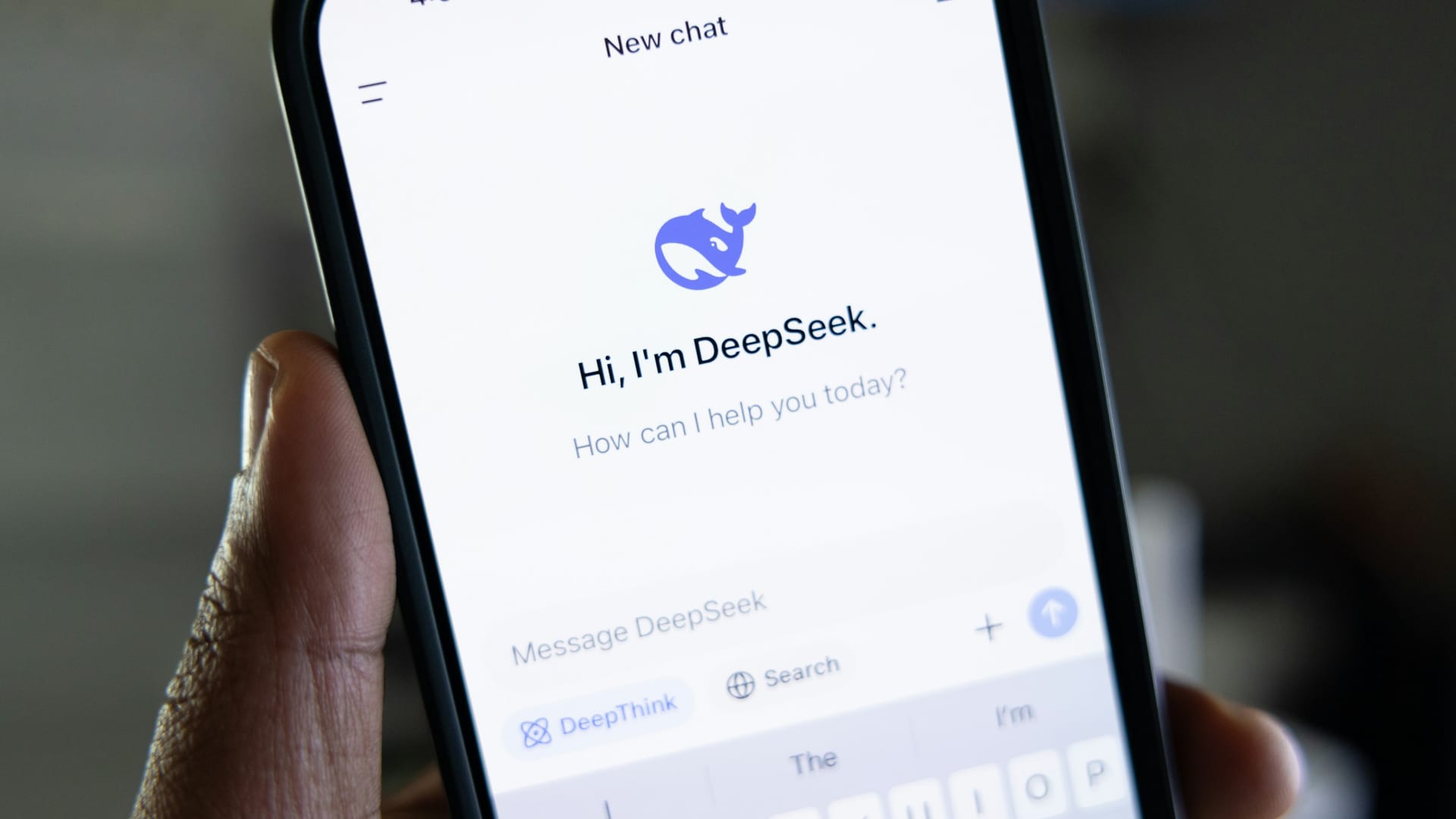 Un móvil en la mano con la app de DeepSeek abierta, con su saludo y los botones de pensar y buscar
