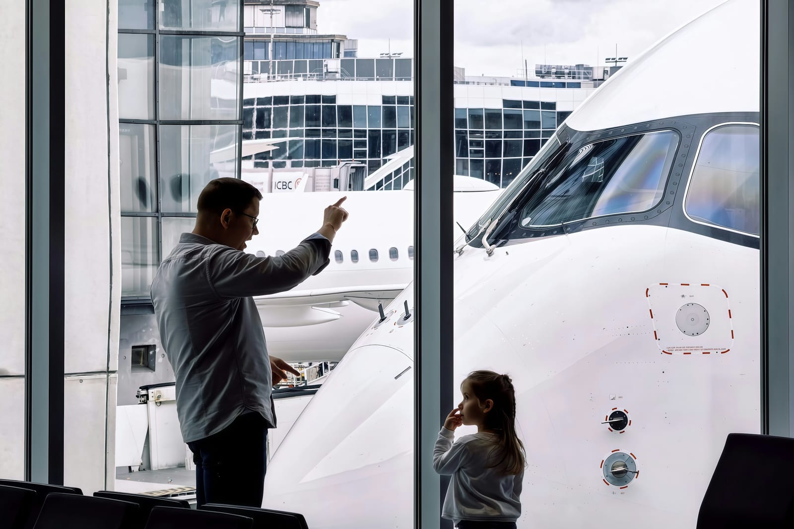 Un padre y su hija miran un avión desde la ventana de la puerta de embarque