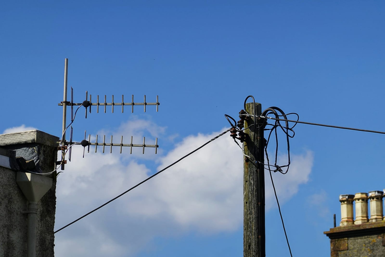 Antenas de televisión en una fachada y un poste, con chimeneas y un cielo azul con nubes