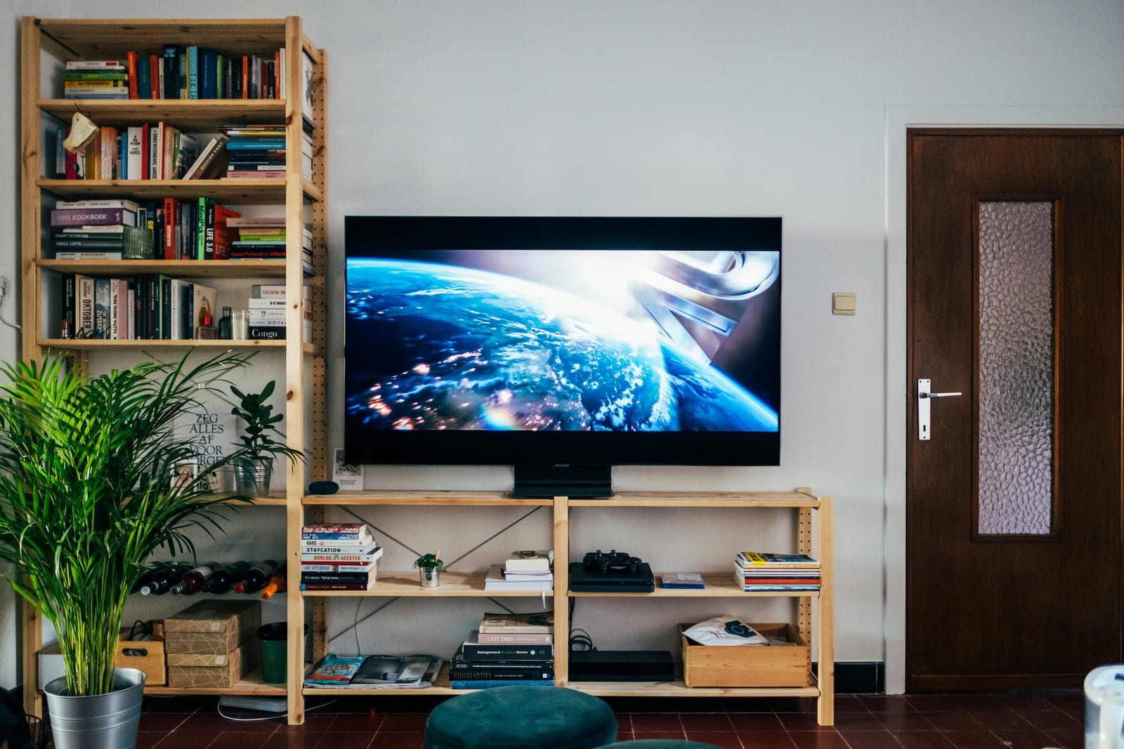 Una tele grande encendida en una estantería de madera, junto a libros y una planta