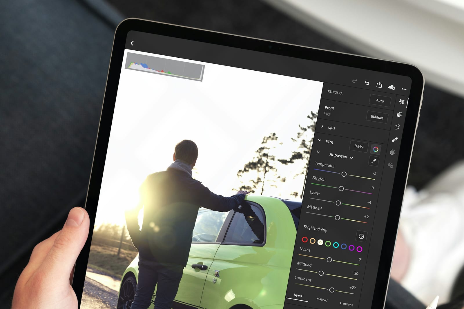 Una mano sostiene una tableta con una app de edición de fotos abierta, con la imagen de un hombre junto a un coche verde