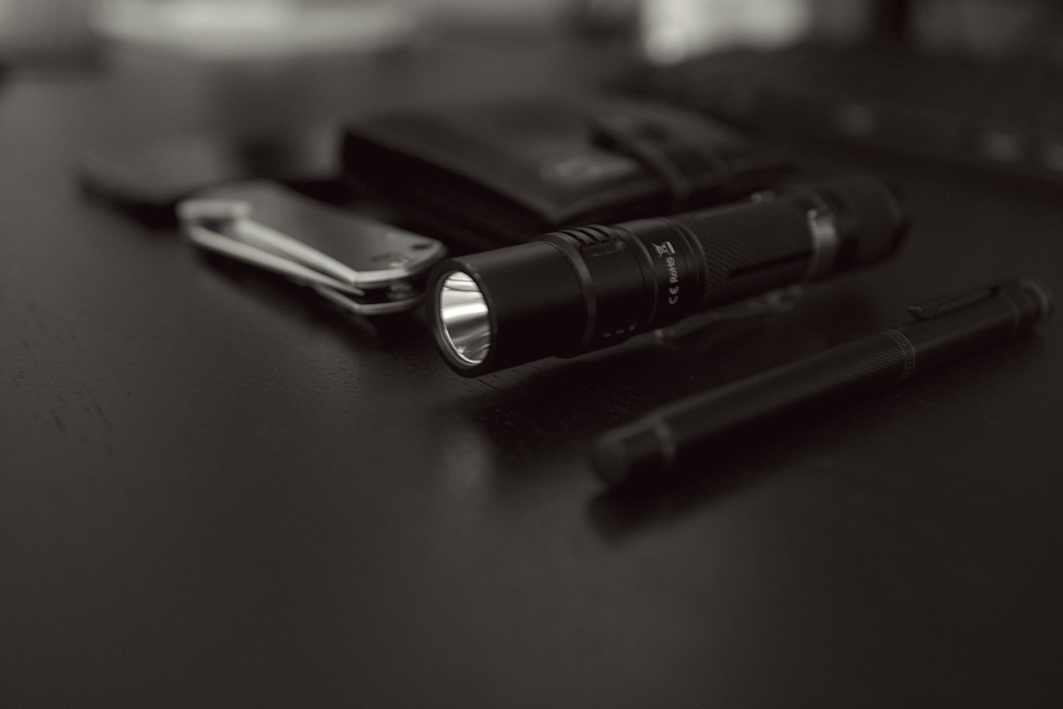 Una linterna encendida sobre una mesa oscura, junto a una navaja y un bolígrafo