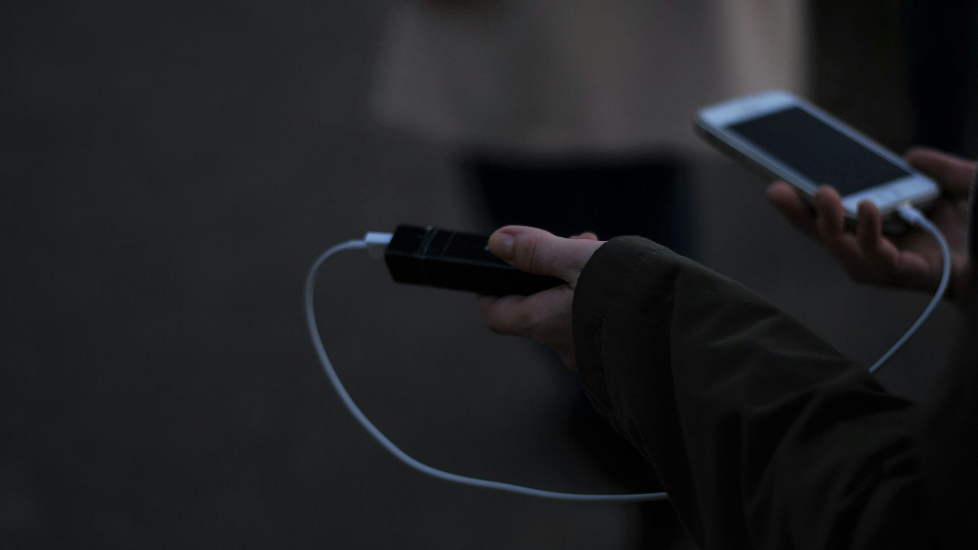 Un móvil cargándose de un power bank a oscuras, sujeto con las dos manos