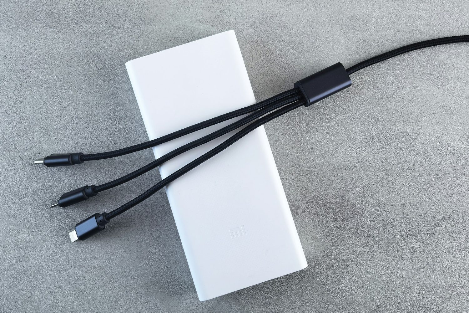 Un power bank blanco con tres cables de carga sobre una superficie gris