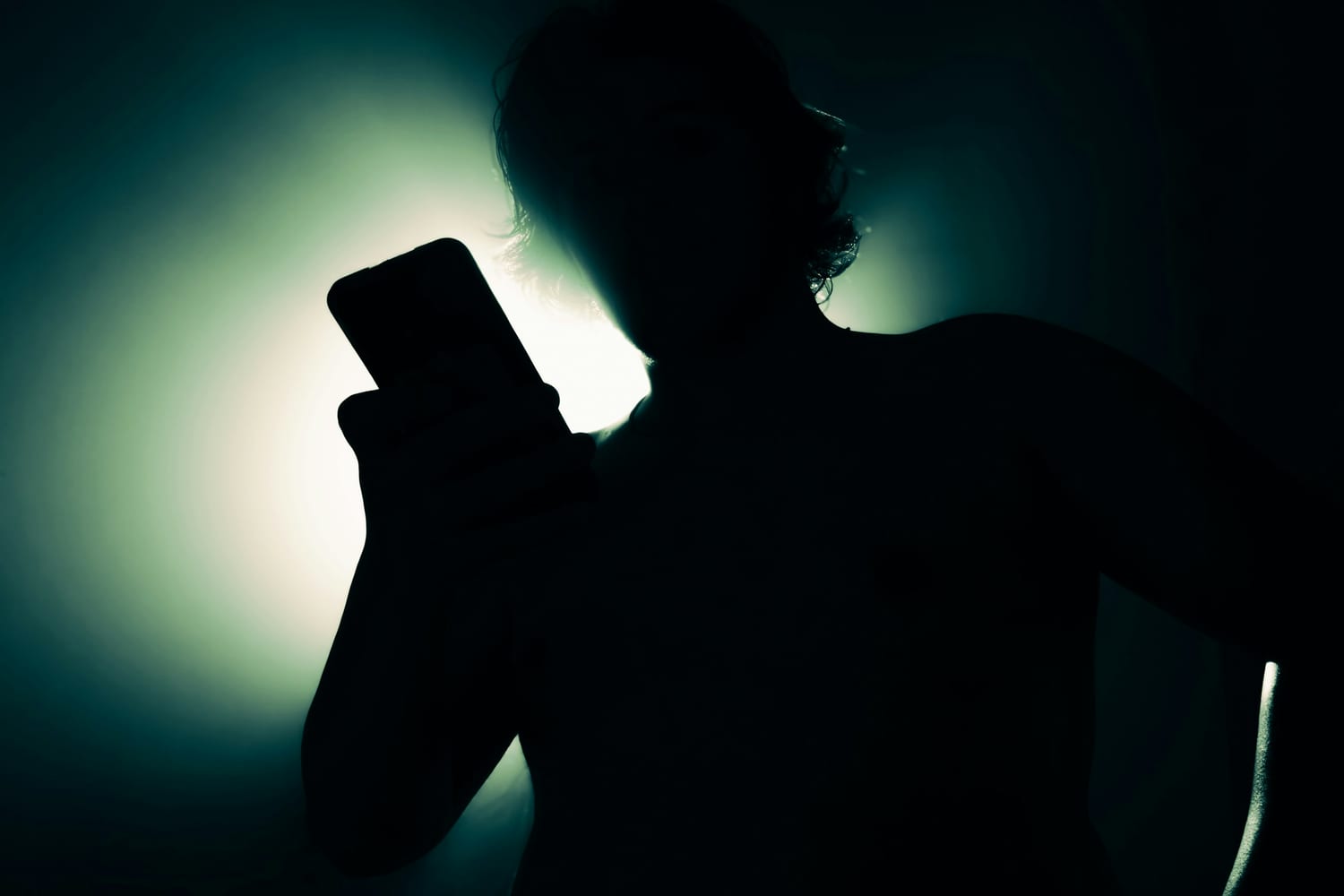 La silueta de una persona a contraluz mirando su móvil