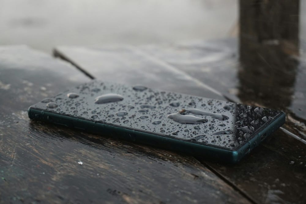 Móvil cubierto de gotas de agua sobre una mesa de madera mojada