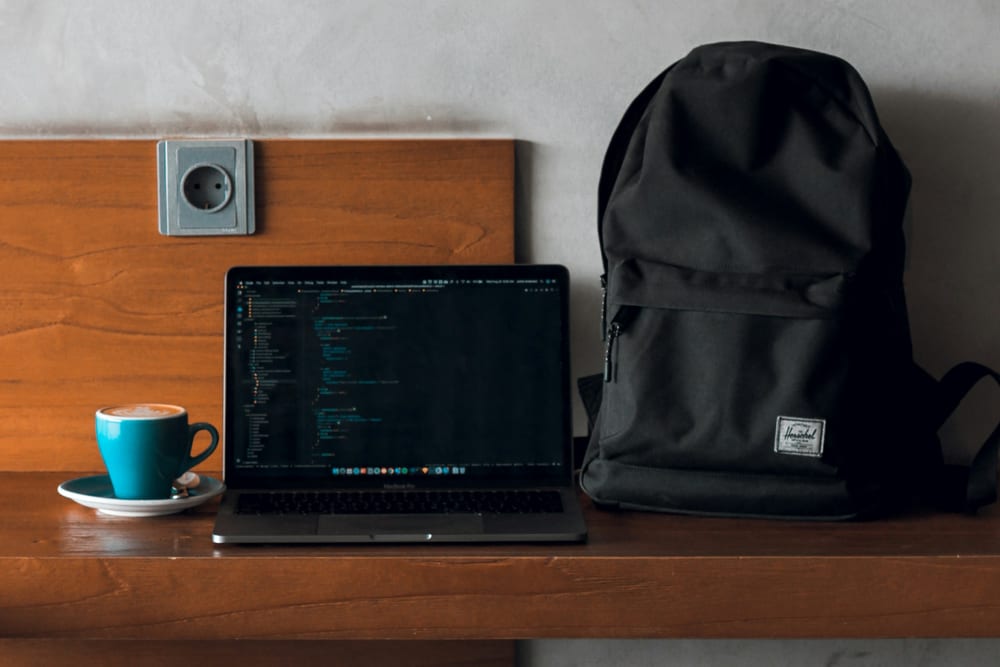 Portátil abierto sobre una mesa de madera junto a una mochila y una taza