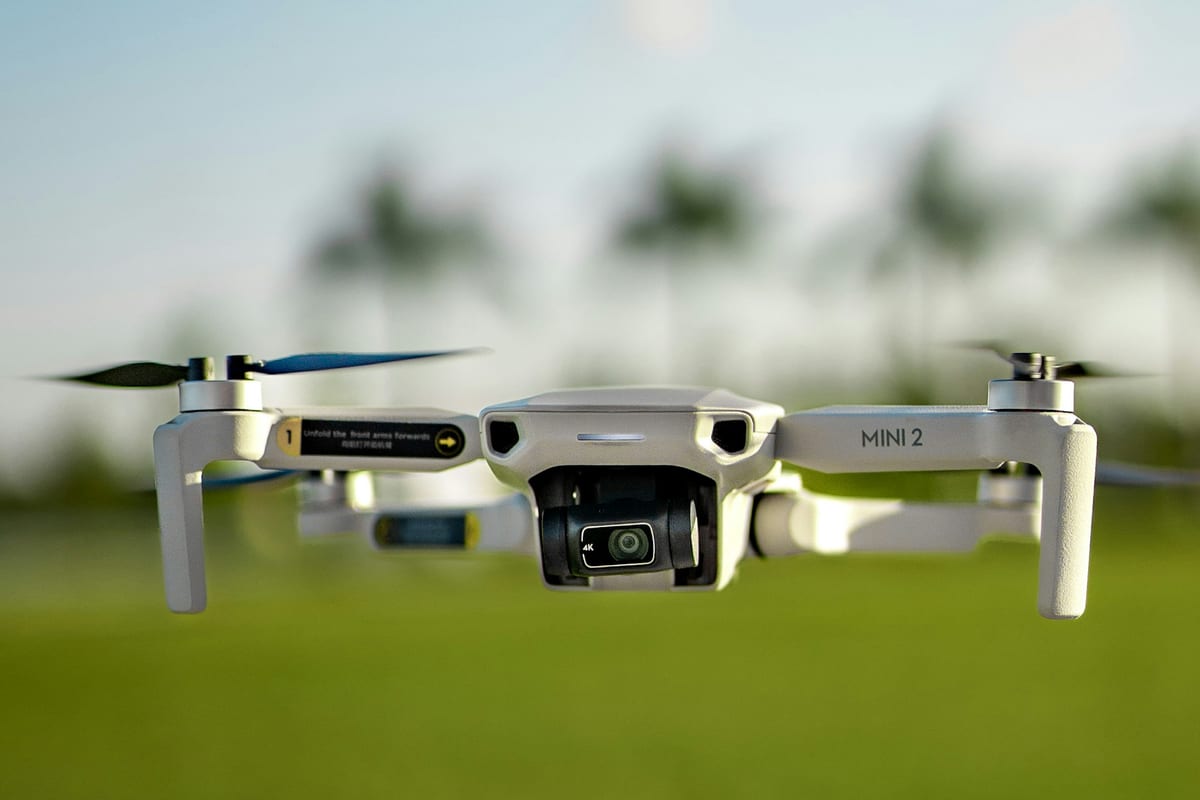 Un DJI Mini 2 vuela a poca altura sobre un campo de hierba con palmeras al fondo