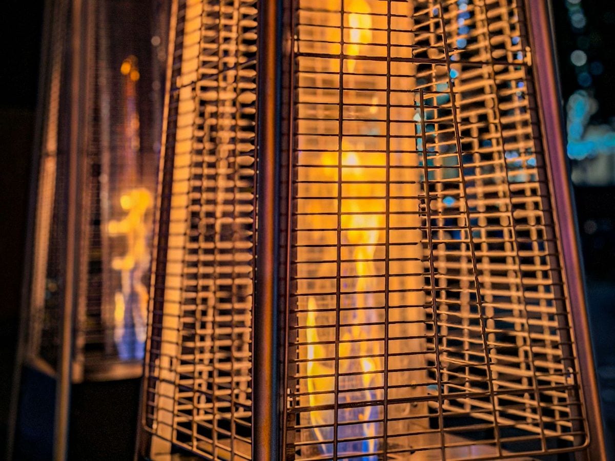 Estufa de gas de exterior de tipo pirámide con la llama dentro de un tubo de cristal, de noche