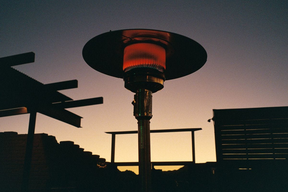 Estufa de gas de exterior de tipo seta encendida en una terraza al atardecer