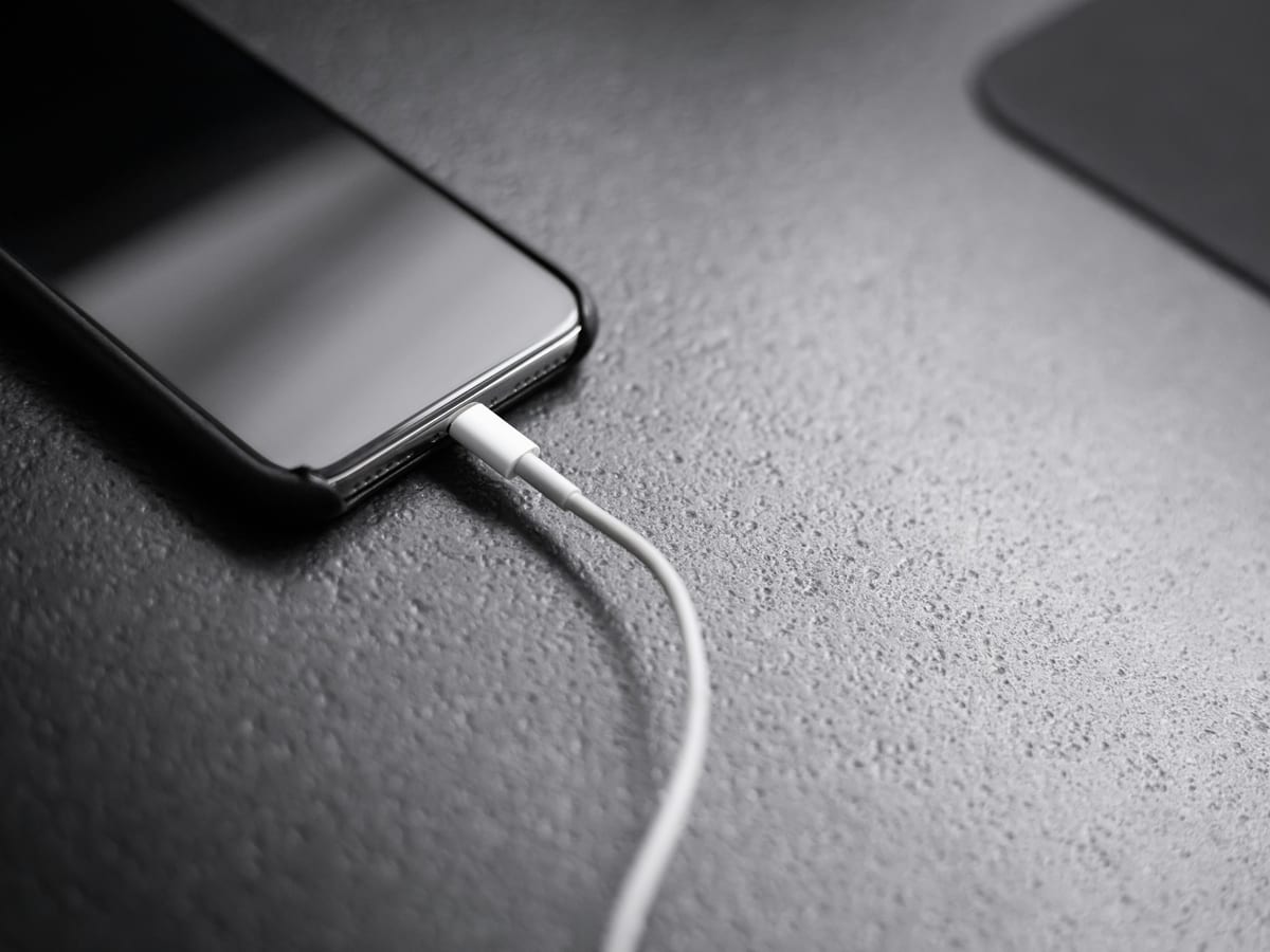 Móvil negro cargando con un cable blanco sobre una mesa gris
