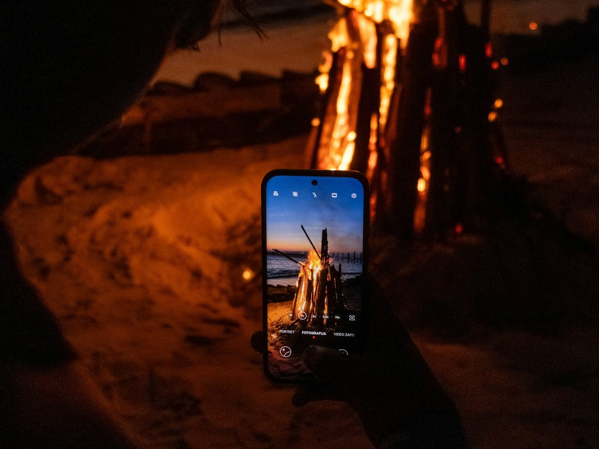 Móvil haciendo una foto de una hoguera en la playa de noche, con la escena iluminada en la pantalla