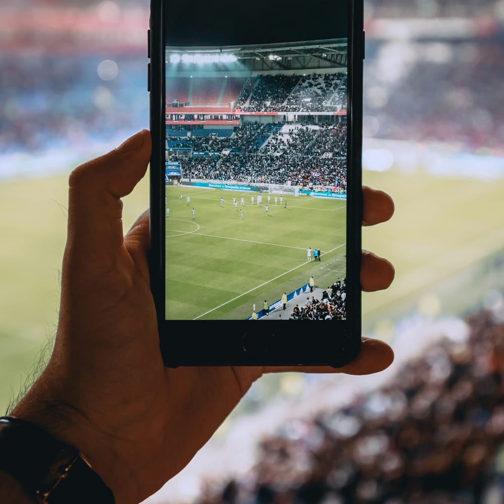 Mano haciendo una foto de un estadio de fútbol con el móvil