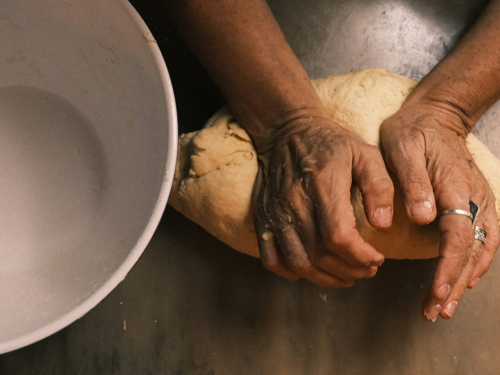 Manos amasando una bola de masa de pan junto a un cuenco blanco