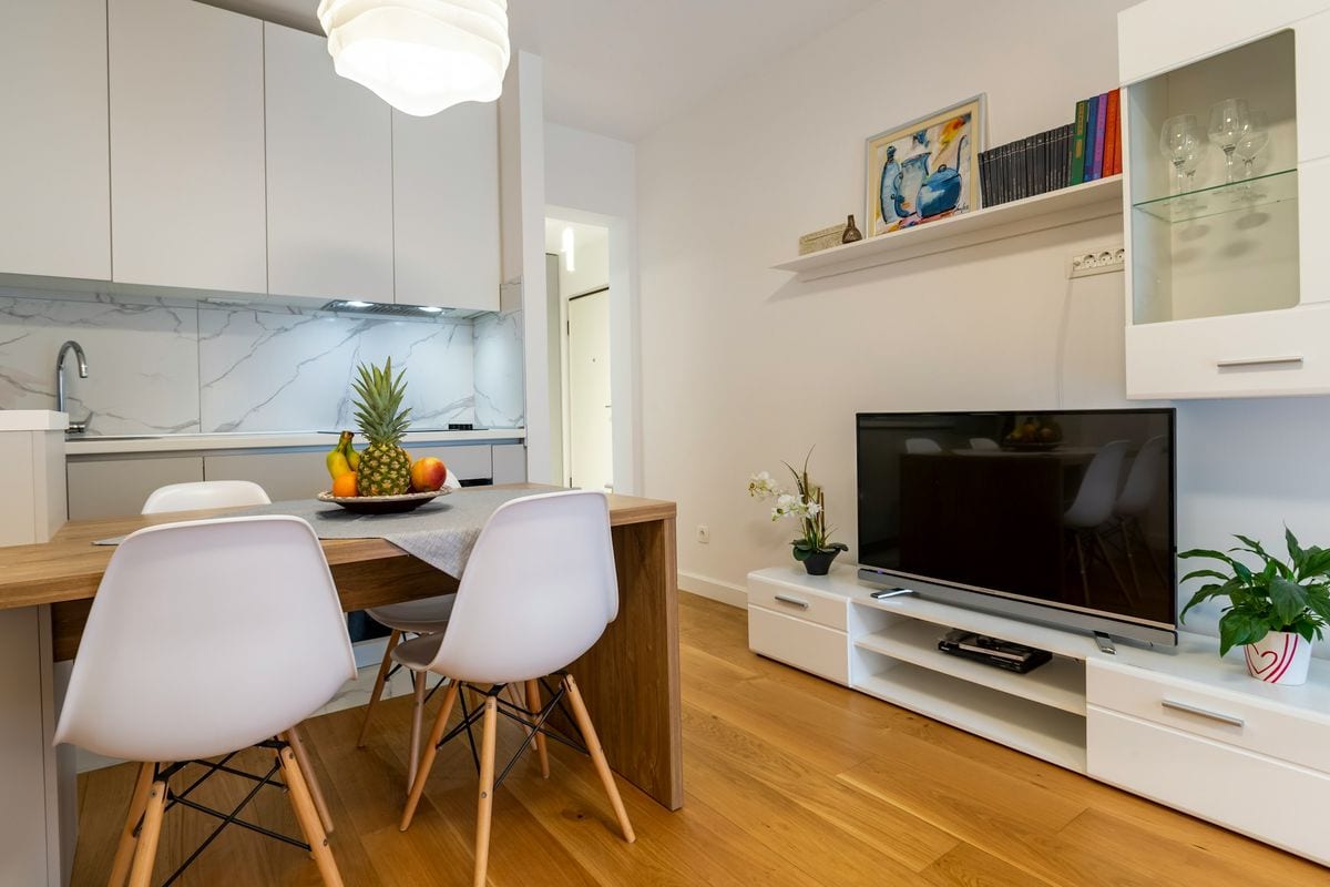 Cocina abierta con una mesa blanca y un televisor sobre un mueble bajo
