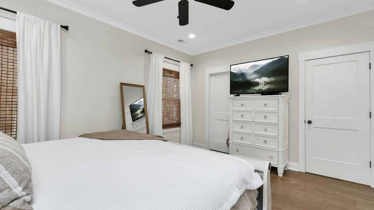 Dormitorio con una cama blanca y un televisor encima de una cómoda blanca, enfrente
