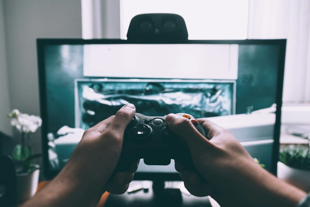 Manos con un mando de consola delante de una pantalla, en un escritorio