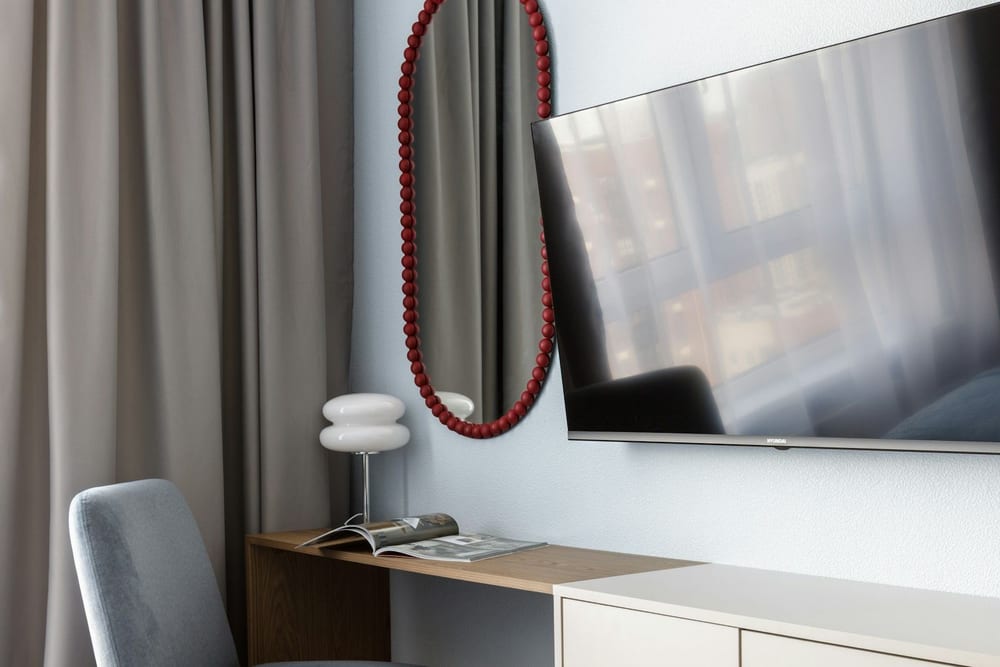 Dormitorio con un televisor colgado en la pared encima de una cómoda clara y un espejo
