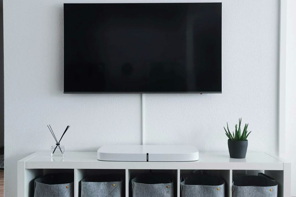 Televisor apagado colgado en una pared blanca, sobre un mueble bajo con una barra de sonido
