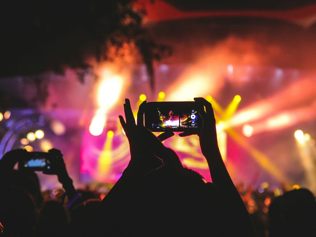 Manos levantando un móvil para grabar un concierto entre luces de escenario