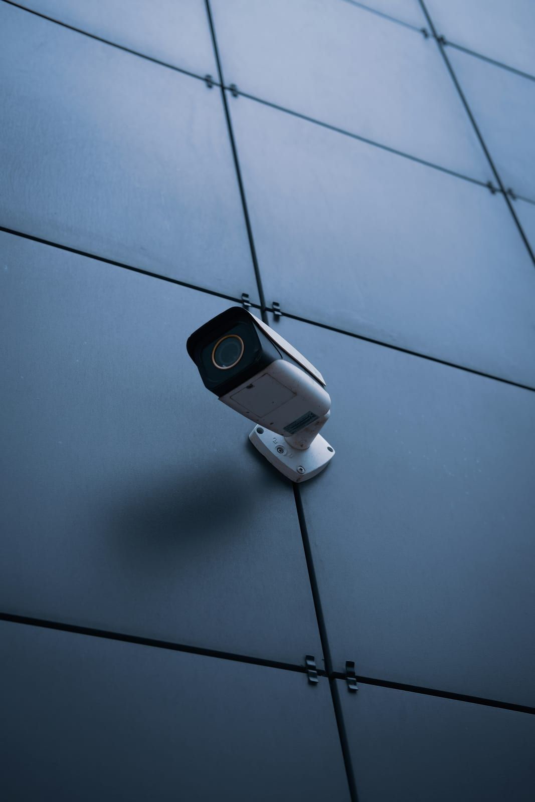 Cámara de seguridad blanca en la esquina de una fachada de paneles oscuros