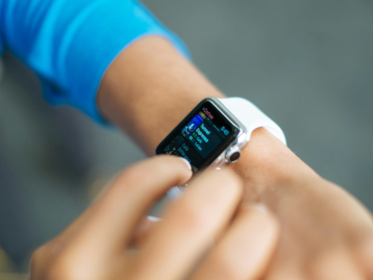 Una mano toca la pantalla de un Apple Watch de aluminio con correa blanca para leer un aviso