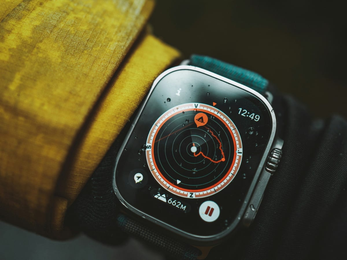 Un Apple Watch Ultra con la brújula en pantalla, en la muñeca de alguien con chaqueta de montaña bajo la lluvia