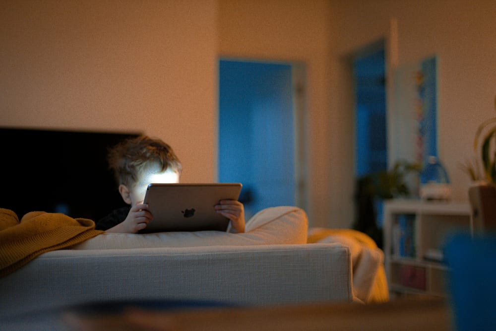 Una persona en el sofá, de noche, viendo algo en un iPad apoyado en las rodillas