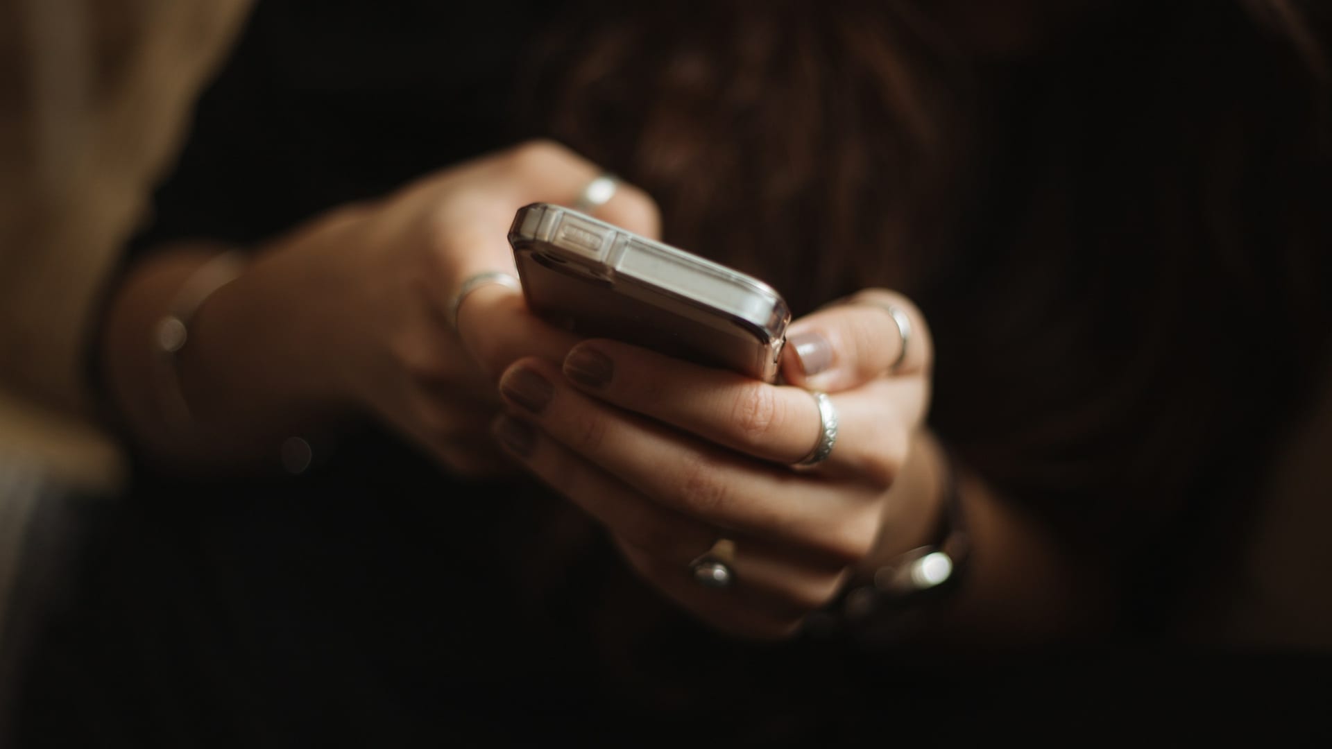 Las manos de una persona sostienen un móvil y leen un mensaje en la penumbra