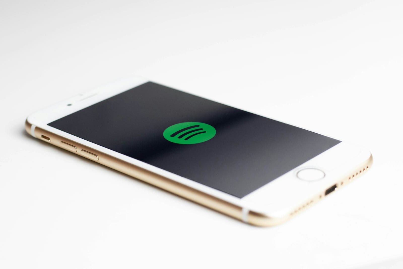 Un iPhone dorado con el logotipo de Spotify en la pantalla sobre una mesa blanca