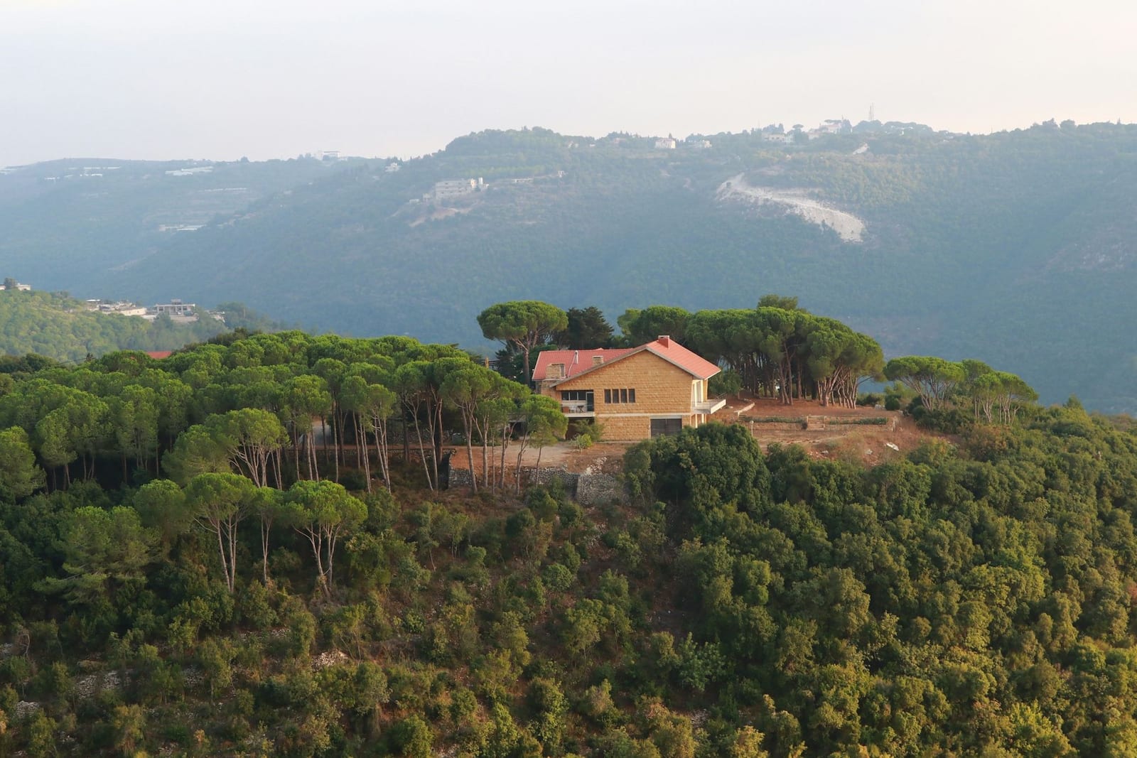 Una casa de piedra con tejado rojo en lo alto de una ladera cubierta de pinos