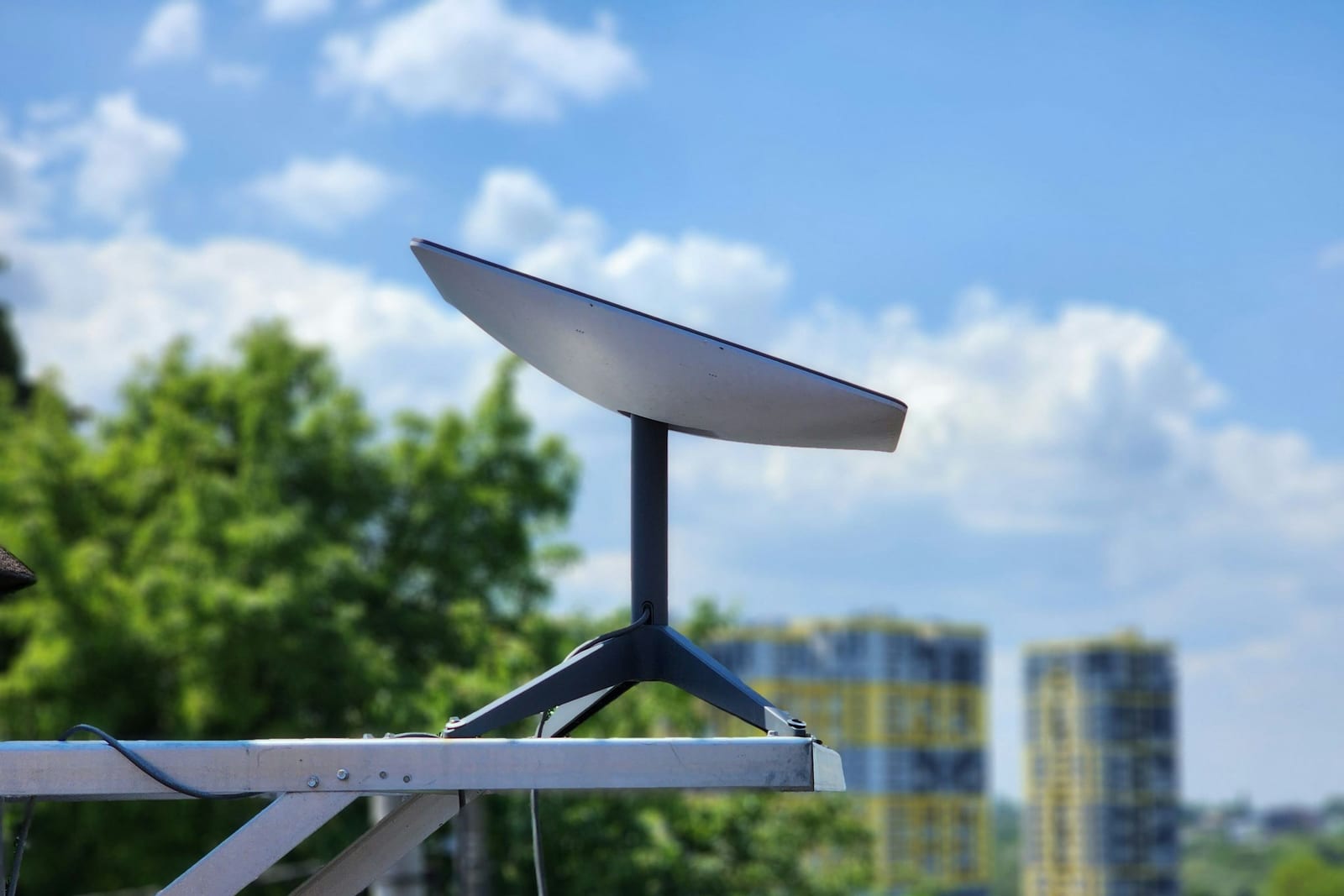 Una antena Starlink de las de casa montada en un mástil sobre la barandilla de un balcón, con el cielo azul detrás