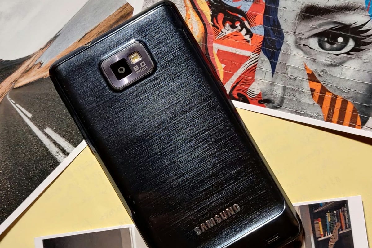 La parte de atrás de un móvil Samsung negro de hace más de diez años, sobre unas fotos impresas