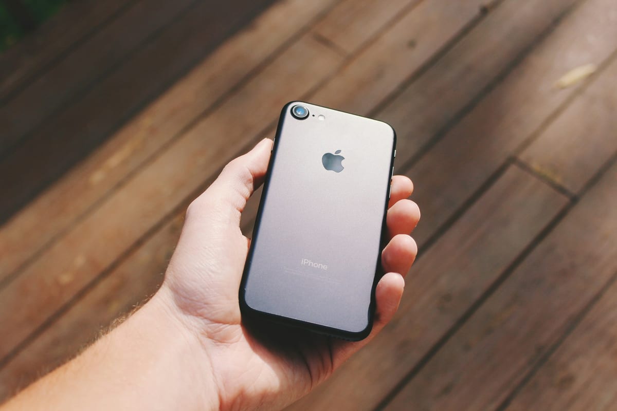 Una mano sujeta un iPhone 7 negro por detrás, sobre un suelo de madera